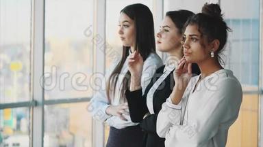 办公室里有三位年轻漂亮的黑发商务小姐。 严肃认真，双手交叉着看着旁边